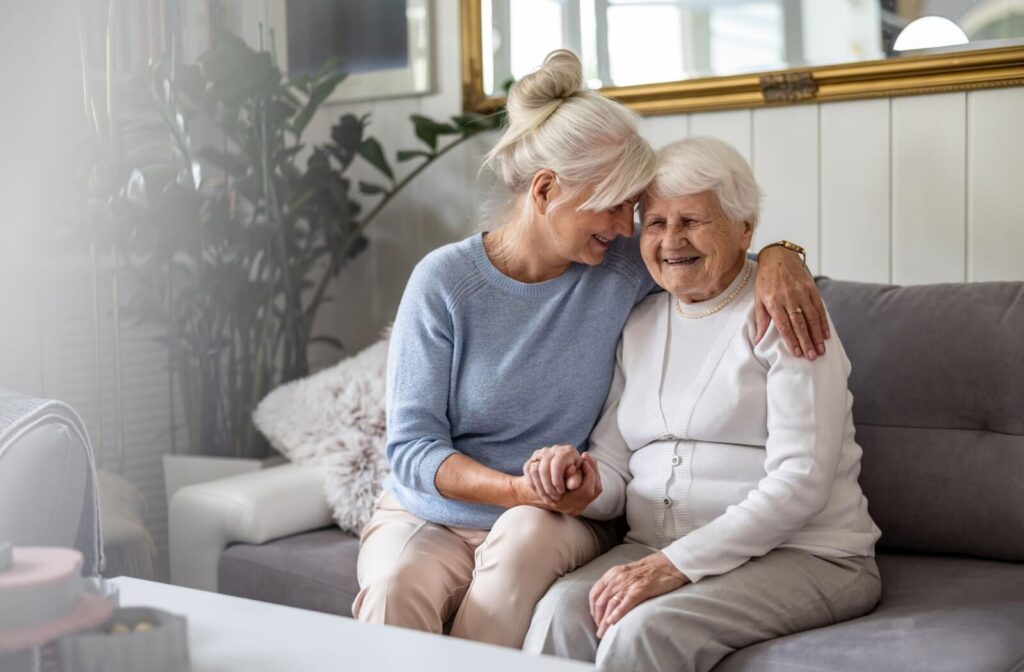 An older adult visiting their aging parent in memory care, hugging and smiling on the couch.
Dan Hendrikx