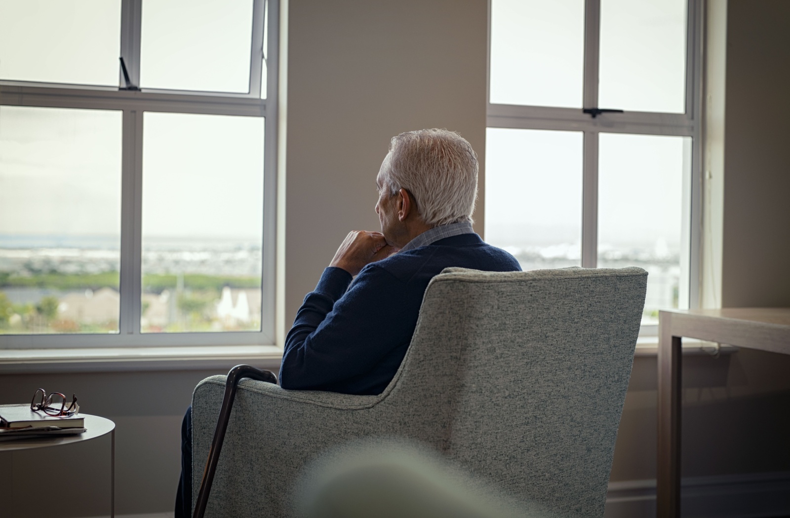 A lonely senior sits in an armchair, staring out the window, feeling isolated by their lack of social connections