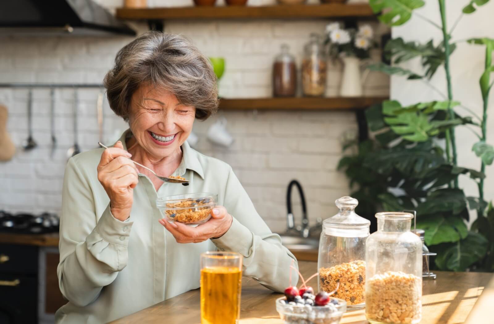 Senior sitting in a bright kitchen enjoying a healthy snack of cereal and fruit