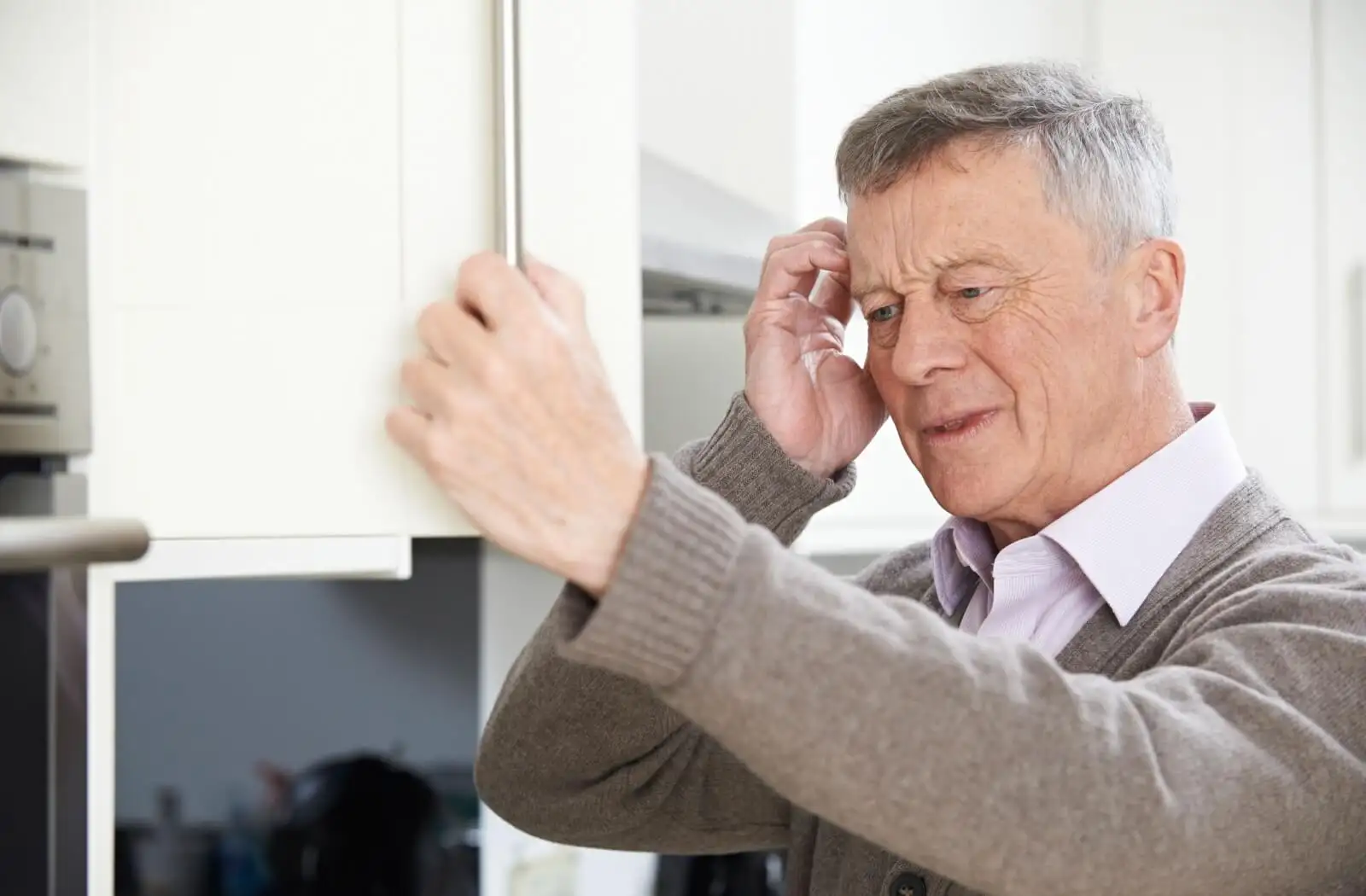 Elderly man looking confused while reaching for a kitchen cabinet, showcasing moments of everyday life and the challenges of aging.