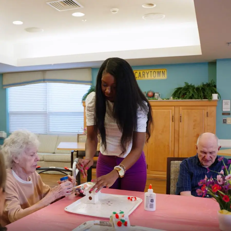 Caregiver assisting elderly residents with a craft activity at a senior living community, fostering creativity and social interaction.