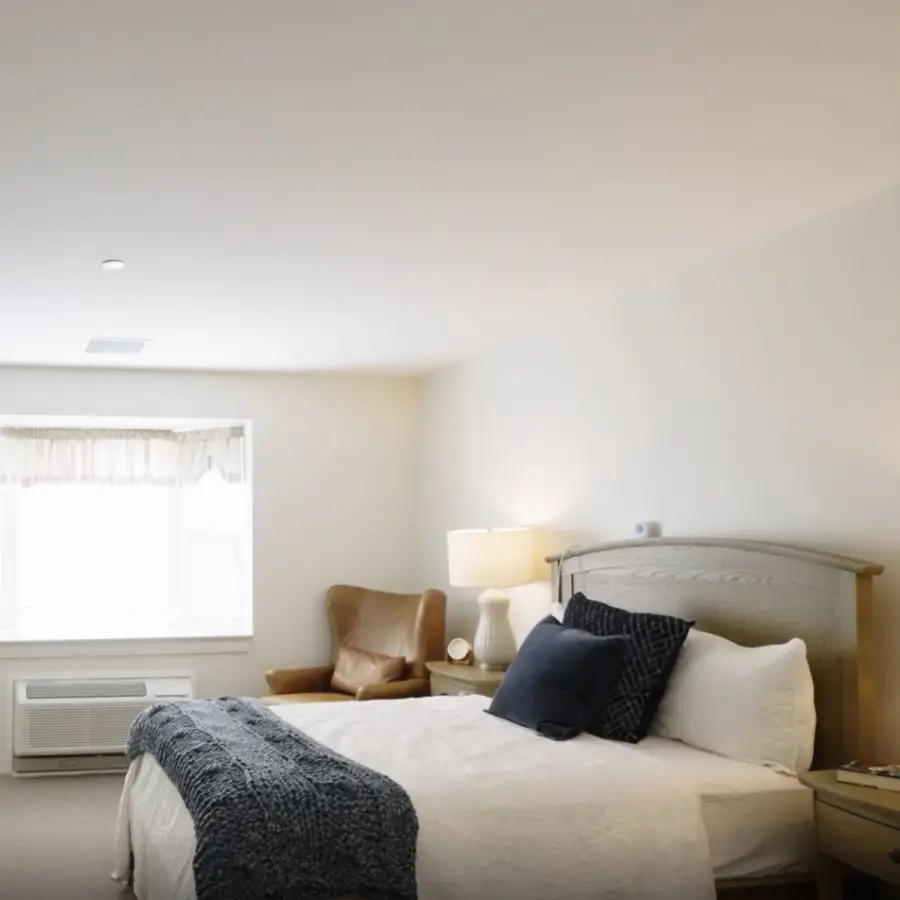 Modern hotel bedroom featuring a comfortable queen-sized bed with decorative pillows, a cozy armchair, and natural light from a window, creating a welcoming atmosphere.
