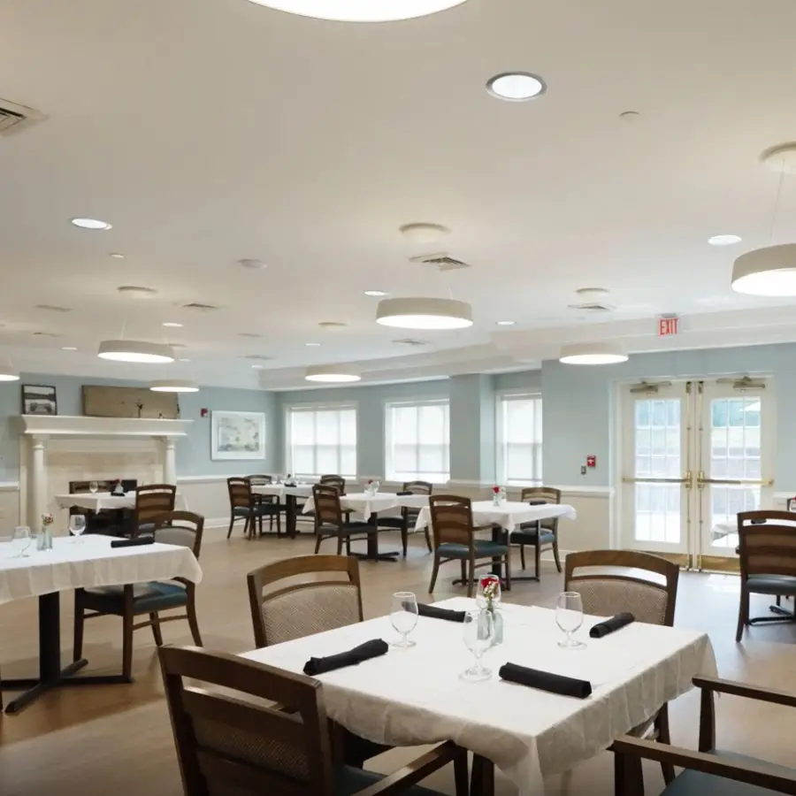 Modern dining area featuring wooden chairs and elegantly set tables with white tablecloths, bright natural light streaming through large windows, and contemporary lighting fixtures.