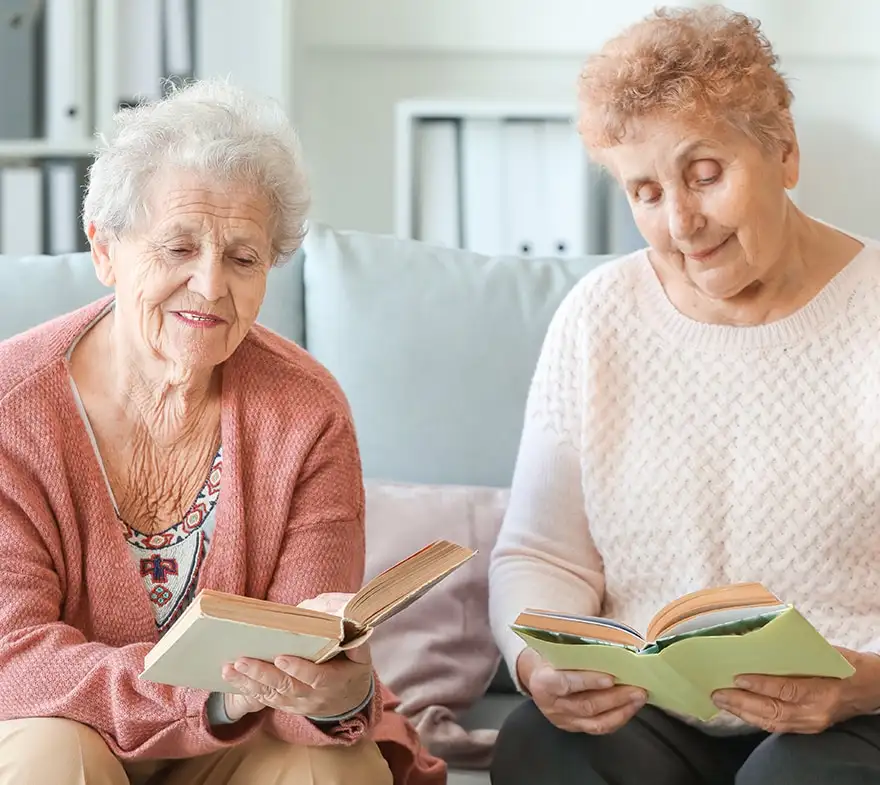 Two elderly women reading books together in a cozy living room, promoting friendship and the joy of reading.