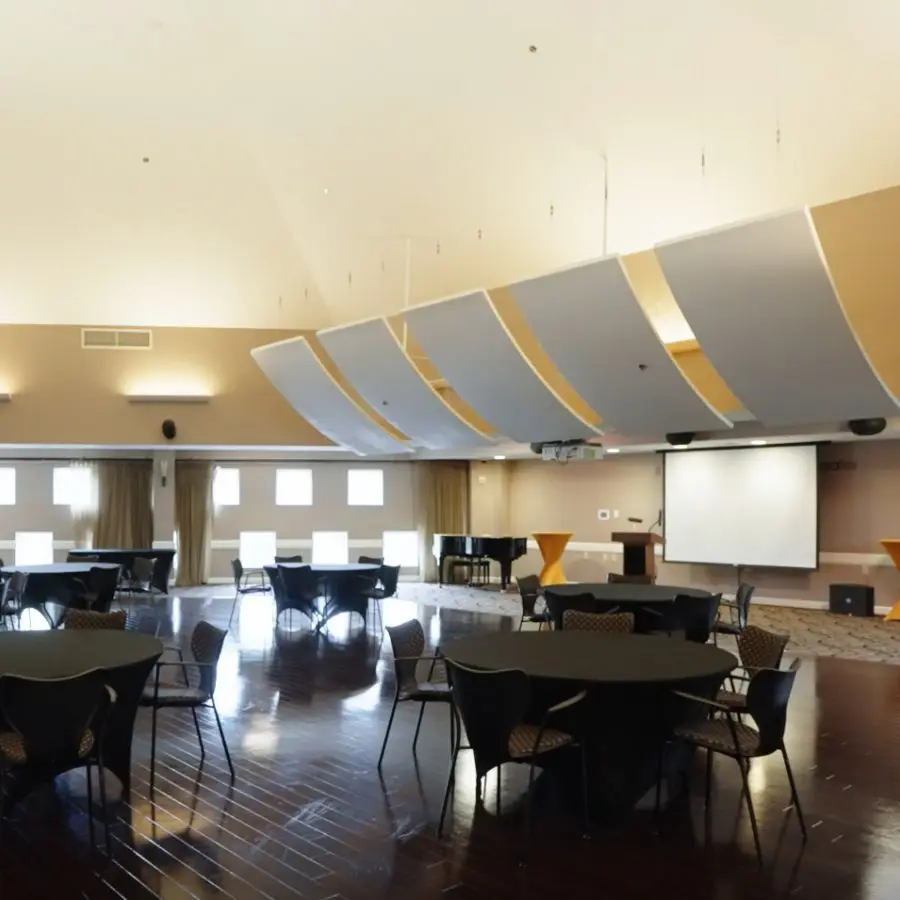 Spacious conference room with round tables and chairs, featuring a large projector screen and modern acoustic paneling on the ceiling. Ideal for meetings and events.
